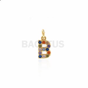 Puede incluir: Encanto de oro en forma de la letra B, con piedras preciosas de colores engastadas en el metal.