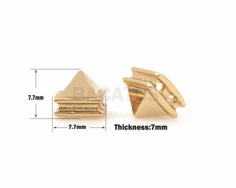 Puede incluir: Dos tachuelas de metal en forma de pirámide de color dorado con una base de 7,7 mm y un grosor de 7 mm. Las tachuelas tienen una superficie texturizada y un pequeño agujero en la parte superior.
