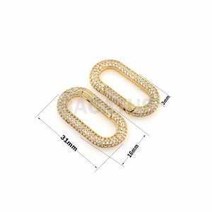 May include: Two gold-toned oval-shaped clasps with clear rhinestones. The clasps are 31 mm long and 16 mm wide.