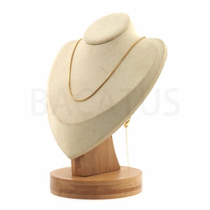 Può includere: Una collana a catena dorata esposta su un busto in velluto beige con una base in legno.