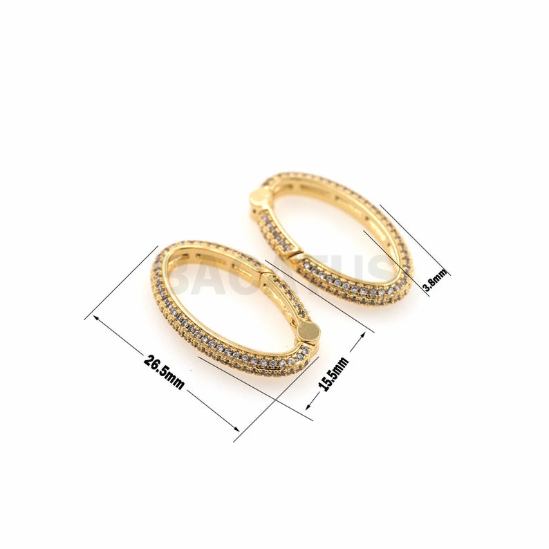 May include: Two gold oval-shaped clasps with clear cubic zirconia stones. The clasps are 1.55 inches long and 0.38 inches wide.
