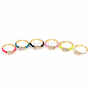 May include: Seven gold rings with a clear gemstone and colorful enamel accents. The rings are in the colors pink, turquoise, black, light pink, yellow, white, and red.