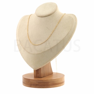 May include: A gold chain necklace displayed on a beige velvet bust with a wooden base.