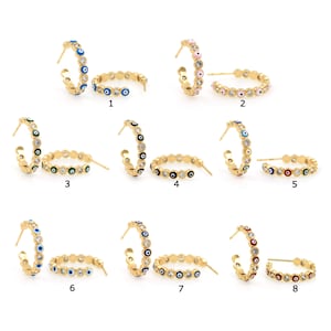 May include: Eight pairs of gold hoop earrings featuring different coloured evil eye charms. Each pair has a unique colour combination of blue, green, pink, black, red and white.
