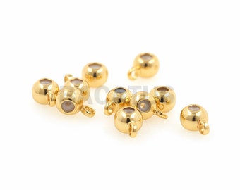 May include: A group of eight gold-coloured metal beads with a small loop on each bead. The beads have a clear centre with a white interior.