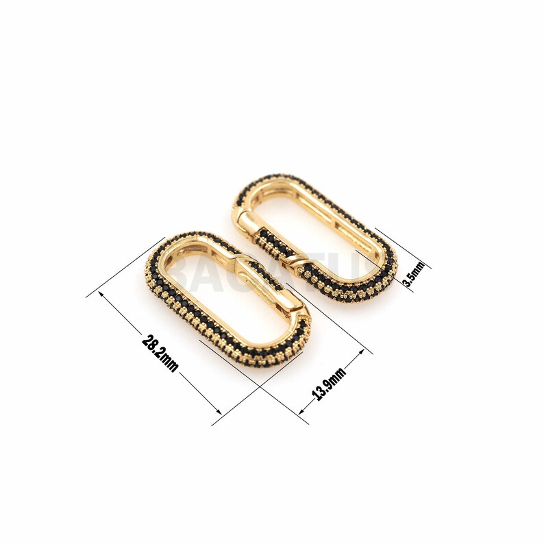 May include: Two gold-toned oval-shaped clasps with black accents. The clasps are 13.9 mm wide and 28.2 mm long.