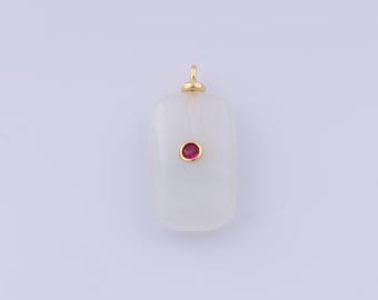 Puede incluir: Un colgante rectangular con bordes redondeados. El colgante es blanco con una pequeña gema roja redonda engastada en un bisel dorado. Un lazo dorado en la parte superior para una cadena.