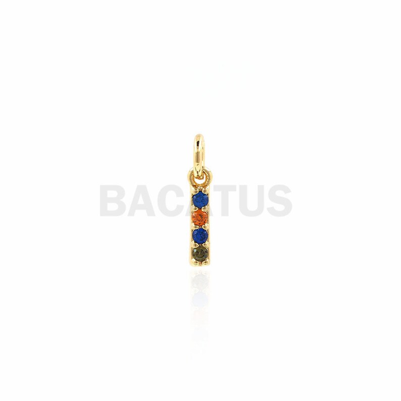 Puede incluir: Encanto de oro con una fila vertical de cinco piedras preciosas de colores. Las piedras preciosas son azules, naranjas, azules, naranjas y verdes.