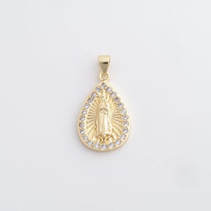 May include: Gold-colored pendant in a teardrop shape, featuring a religious figure in the center. The pendant is outlined with small, clear gemstones. The bail is also gold-colored. The pendant is likely made of metal and is designed to be worn as jewelry.