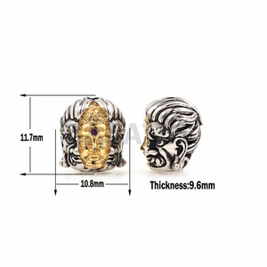 May include: A silver and gold bead with two faces, one with a fierce expression and the other with a serene Buddha face. The bead is 1.17 inches in diameter and 0.43 inches thick.