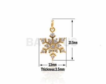 Könnte beinhalten: Goldfarbener Schneeflocken-Anhänger mit klaren, funkelnden Kristallen. Der Anhänger misst 20,5 mm in der Länge, 13 mm in der Breite und 3,5 mm in der Dicke. Er hat eine Schlaufe zum Befestigen an einer Kette oder einem Armband. Ein Schmuckstück zum Thema Winter.