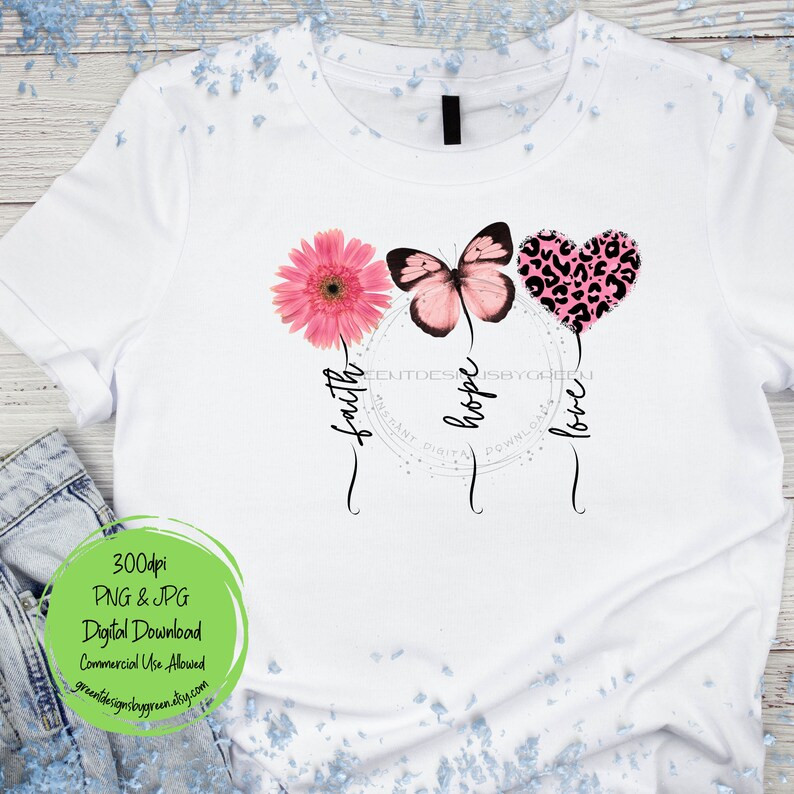 May include: A white t-shirt with a pink butterfly, a pink flower, and a pink heart with a leopard print design. The words "faith", "hope", and "love" are written in a script font below the design.