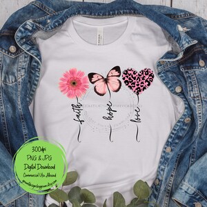 May include: White t-shirt with a pink flower, butterfly, and leopard print heart. The words "faith", "hope", and "love" are written around the design.