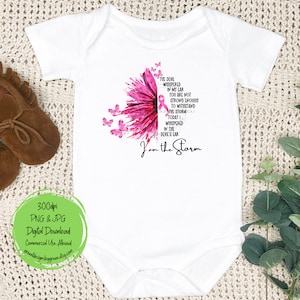 May include: A white baby onesie with a pink watercolor sunflower and a pink ribbon. The text reads "The devil whispered in my ear you are not strong enough to withstand the storm. Today I whispered in the devil's ear I am the storm."