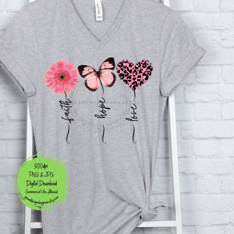 May include: A gray t-shirt with a pink flower, butterfly, and heart with a leopard print design. The words "faith", "hope", and "love" are written below the design.