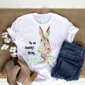 May include: White t-shirt with a brown bunny rabbit holding a stack of teacups with flowers. The text "You are Somebody's Blessing..." is printed on the shirt.