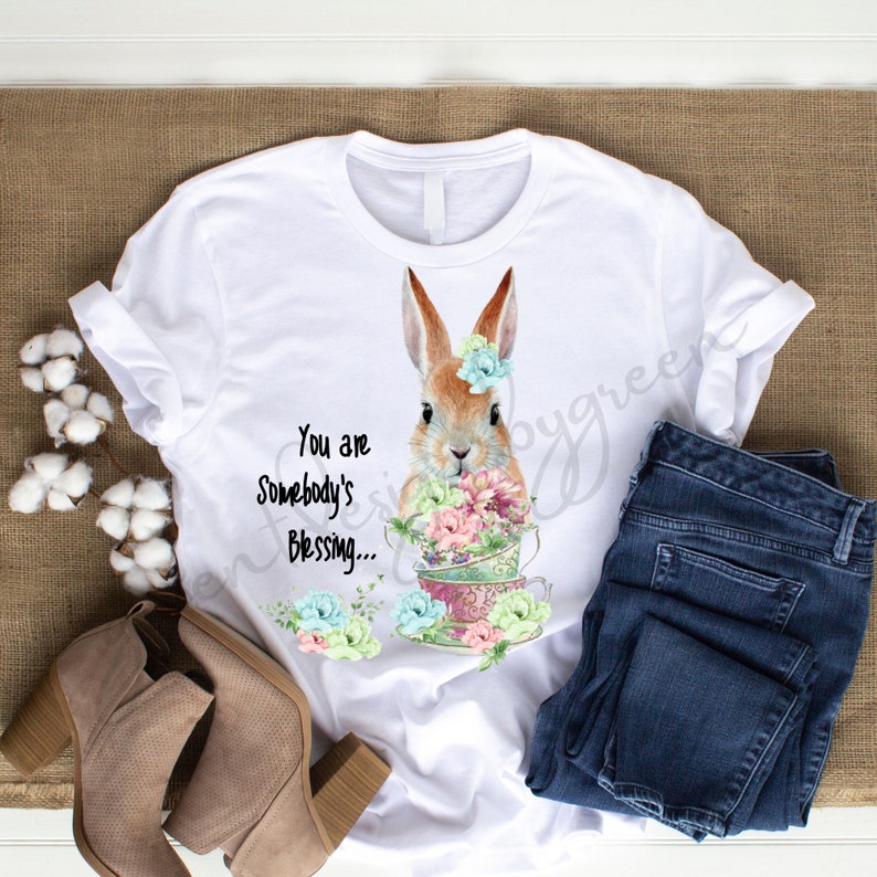 May include: White t-shirt with a brown bunny rabbit holding a stack of teacups with flowers. The text "You are Somebody's Blessing..." is printed on the shirt.