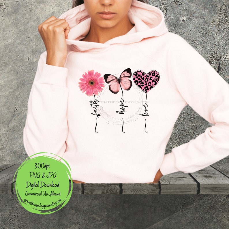 May include: A pink hoodie with a graphic design featuring a pink flower, a butterfly, and a leopard print heart. The graphic is surrounded by a circle with the words "faith", "hope", and "love" written around it.