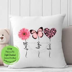 May include: A white pillow with a pink flower, butterfly, and heart with a leopard print design. The words "faith", "hope", and "love" are written around the design.
