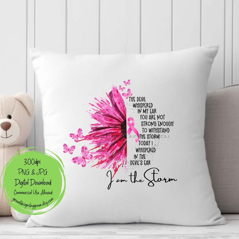 May include: A white pillow with a pink watercolor flower design and a pink ribbon. The text "The devil whispered in my ear you are not strong enough to withstand the storm today I whispered in the devil's ear I am the storm" is printed on the pillow.