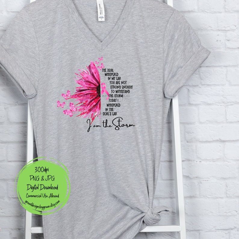 May include: A gray t-shirt with a pink sunflower design and the text "The devil whispered in my ear you are not strong enough to withstand the storm today I whispered in the devil's ear I am the storm".