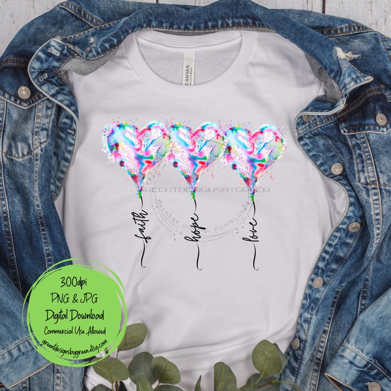 Pode incluir: Uma camiseta branca com um design de tr&ecirc;s bal&otilde;es de cora&ccedil;&atilde;o de aquarela com as palavras "f&eacute;", "esperan&ccedil;a" e "amor" escritas abaixo. Os bal&otilde;es s&atilde;o em tons de rosa, azul e verde.