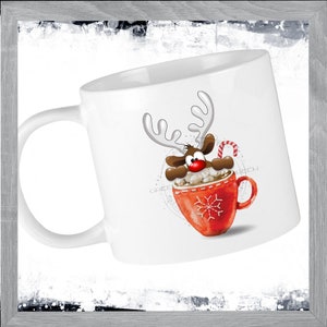 May include: White ceramic mug with a red and white reindeer design. The reindeer is peeking out of a red mug with a snowflake design and holding a candy cane.