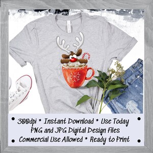 May include: A gray t-shirt with a digital design of a cartoon reindeer peeking out of a red mug with marshmallows and a candy cane. The text "300dpi * Instant Download * Use Today PNG and JPG Digital Design Files Commercial Use Allowed * Ready to Print" is printed below the design.
