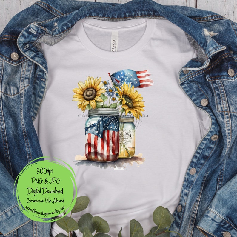 May include: Two mason jars with sunflowers and a small American flag. The jars are decorated with an American flag design. The background is a white t-shirt.