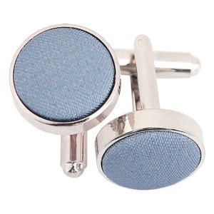May include: A pair of silver cufflinks with a light blue fabric insert. The cufflinks are round and have a smooth, polished finish.