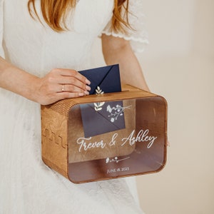 Könnte beinhalten: Eine hölzerne Hochzeitskartenbox mit einem klaren Acryldeckel. Die Box trägt eine personalisierte Inschrift mit dem Text "Trevor & Ashley" und "June 18, 2023".