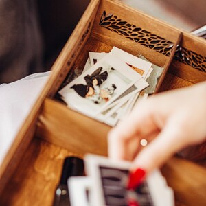 May include: A wooden box with a decorative cutout design, filled with a stack of vintage-style photographs. The photos are in black and white and show a couple.