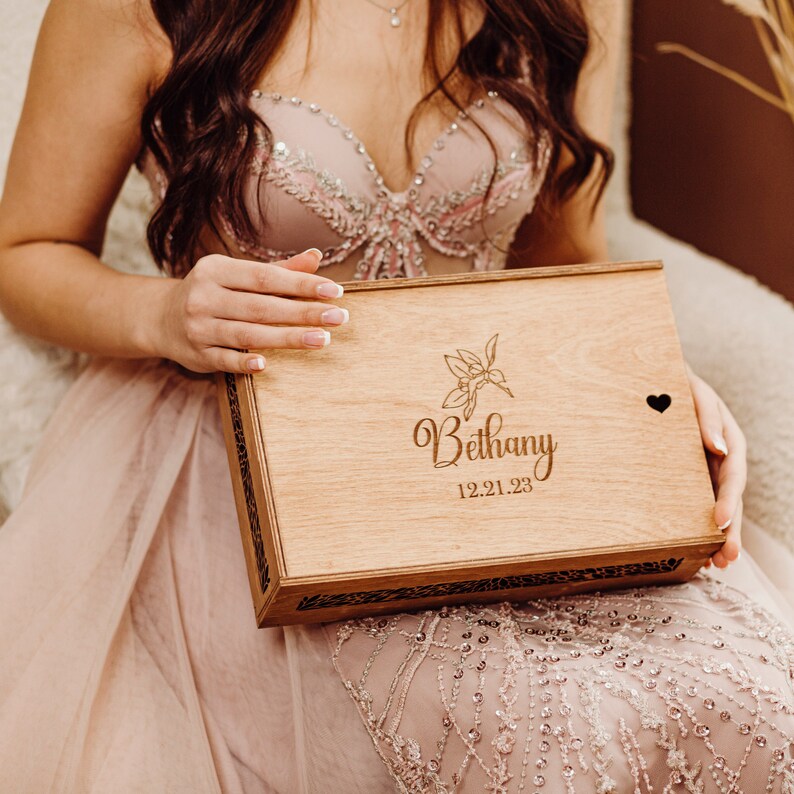 May include: A wooden box with a floral design and the name Bethany engraved on it. The box also has the date 12.21.23 engraved on it.