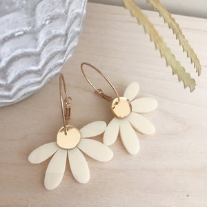May include: A pair of gold hoop earrings with white daisy-shaped charms. The charms have a gold centre.