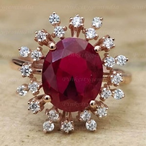 Puede incluir: Un anillo de oro rosa con una gran piedra de rubí ovalada rodeada por un halo de diamantes más pequeños.