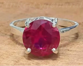May include: A silver ring with a large, round, red gemstone set in a claw setting.