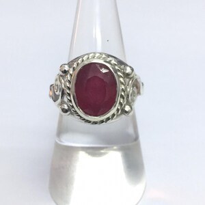 Puede incluir: Un anillo de plata con una piedra preciosa de rubí de forma ovalada engastada en una banda de plata decorativa.