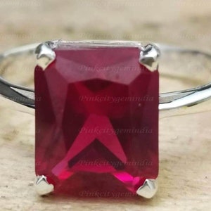 May include: A silver ring with a large, rectangular, deep red gemstone. The gemstone is set in a prong setting.