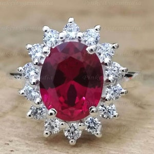 Op de afbeelding: Een zilveren ring met een grote ovale robijn omringd door een halo van kleinere diamanten.
