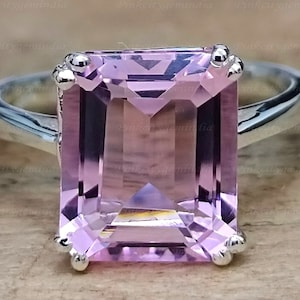 May include: A silver ring with a large, light pink, emerald-cut gemstone. The ring has a simple band and the gemstone is set in a prong setting.