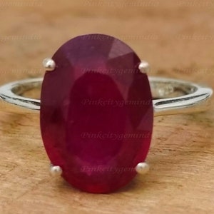 May include: A silver ring featuring a large oval ruby gemstone. The ring is set in a plain band.
