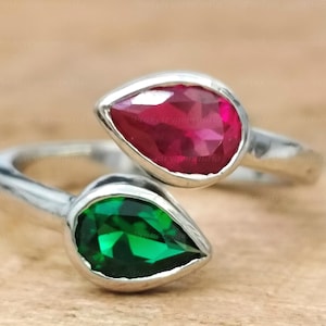 May include: A silver ring with two teardrop-shaped gemstones. The top stone is a vibrant red, and the bottom stone is a deep green.