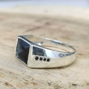 Puede incluir: Un anillo de plata con una piedra rectangular negra y cinco pequeñas piedras negras engastadas en una fila en la banda.