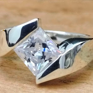 Op de afbeelding: Een zilveren ring met een grote, vierkante, heldere edelsteen gezet in een uniek, hoekig ontwerp.
