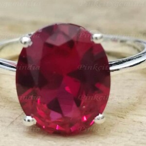 Peut inclure: Une bague en argent avec une grande pierre rouge de forme ovale. La bague est posée sur une surface en bois.