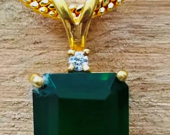 May include: A gold chain necklace with a pendant featuring a large, emerald green gemstone surrounded by a gold setting. A small, clear diamond sits above the gemstone.