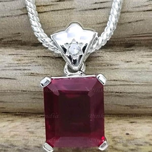 May include: A silver chain necklace with a pendant featuring a large, rectangular, dark red gemstone and a smaller, clear gemstone in a star-shaped setting.