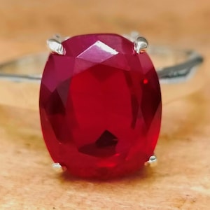 Può includere: Un anello d'argento con una grande pietra rossa di forma ovale.