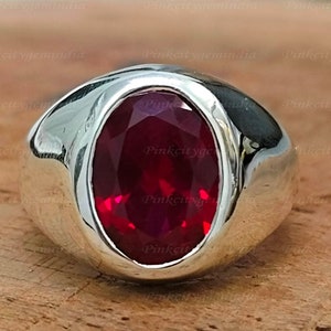 Può includere: Un anello d'argento con una grande pietra preziosa rossa di forma ovale incastonata al centro.