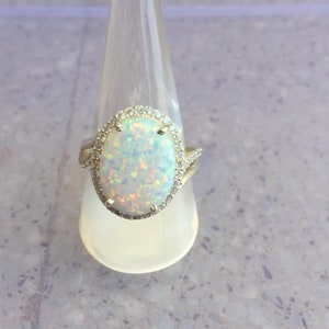 May include: A silver ring with a large oval opal gemstone surrounded by a halo of small clear stones.